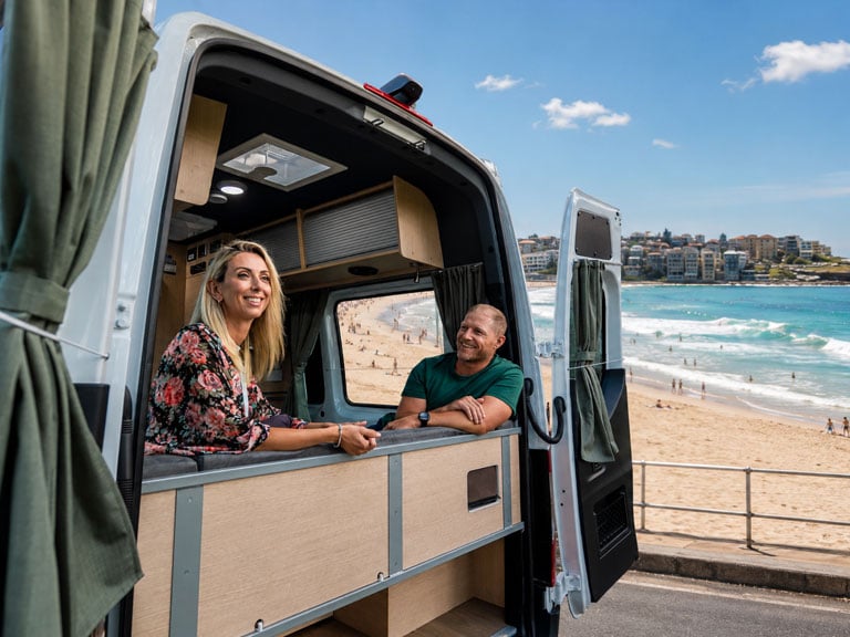 Couple relaxing inside a Maui Ultima motorhome rental at Bondi Beach, Sydney