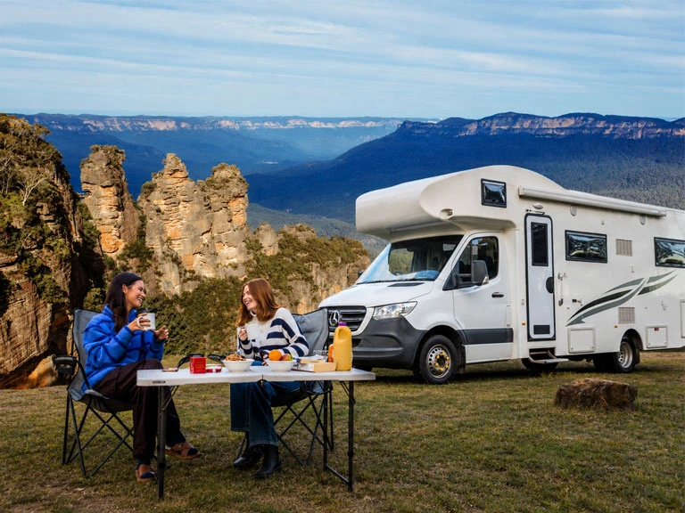 Two travellers having breakfast beside a rented motorhome in the Blue Mountains near Sydney