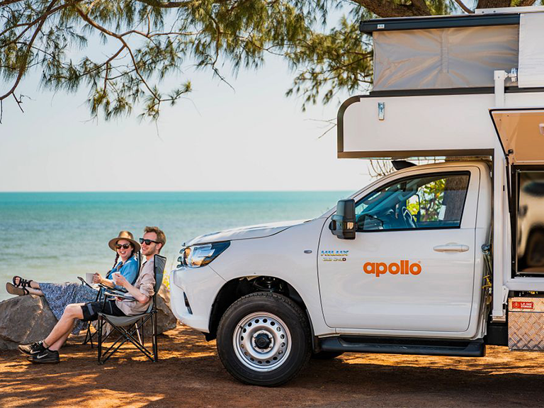 Couple relaxing beside an Apollo 4WD camper near the coast in Darwin