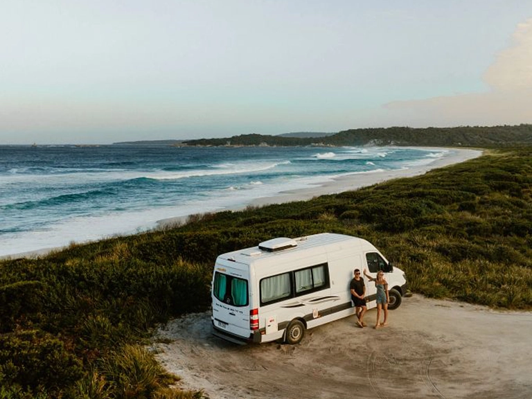Couple beside their campervan overlooking Swimcart Beach on Tasmania’s east coast