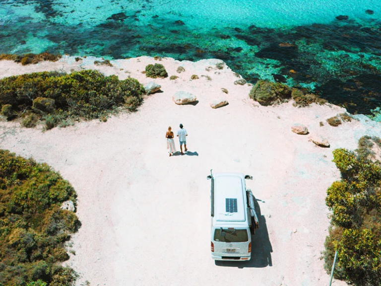 Travellers standing beside their campervan overlooking clear turquoise water on the Australian coast