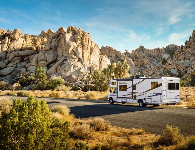 El Monte RV Class C motorhome driving through a rocky desert landscape in California, USA