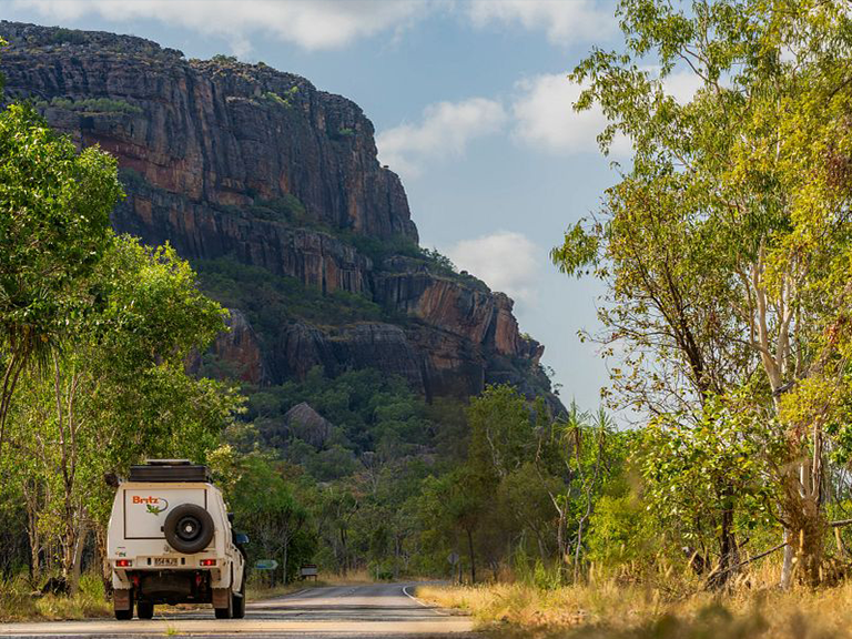 Britz 4WD campervan hire vehicle driving past a sandstone escarpment in the Northern Territory, Australia